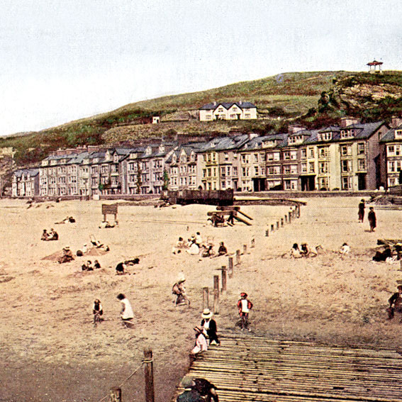 Early 1900's hand coloured photo of Aberdovey beach front, hillside and bandstand taken from the jetty